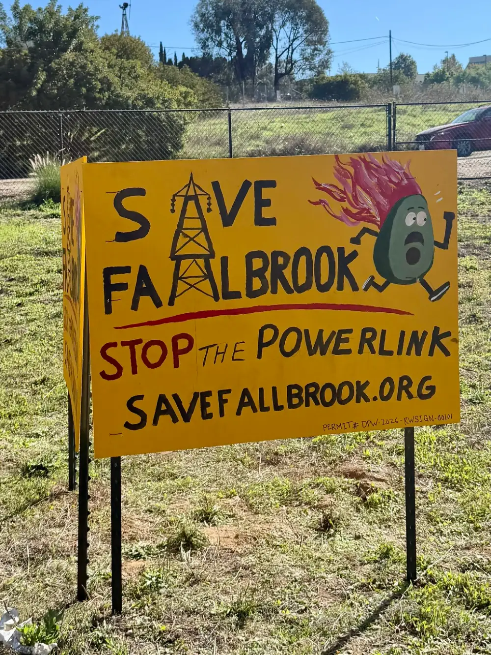 A hand-painted Save Fallbrook sign showing Toast, an avocado with his head on fire, running from a transmission tower